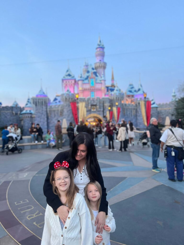 woman and her 2 daughters in front of the castle at disneyland