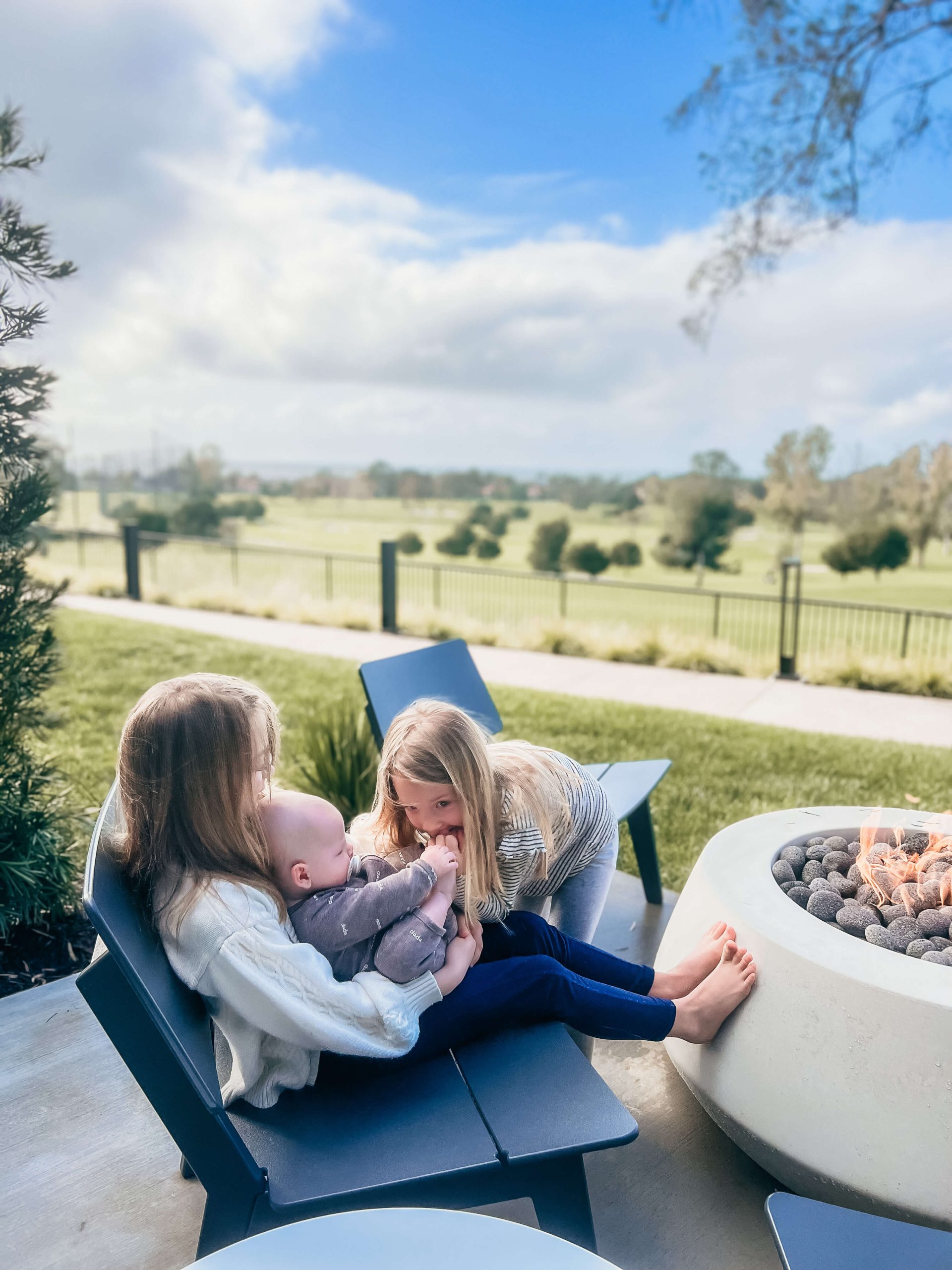 woman holding a baby with her daughter and her feet up on a fire pit outside