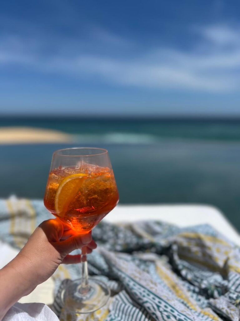 woman's hand holding a cocktail overlooking beach in cabo