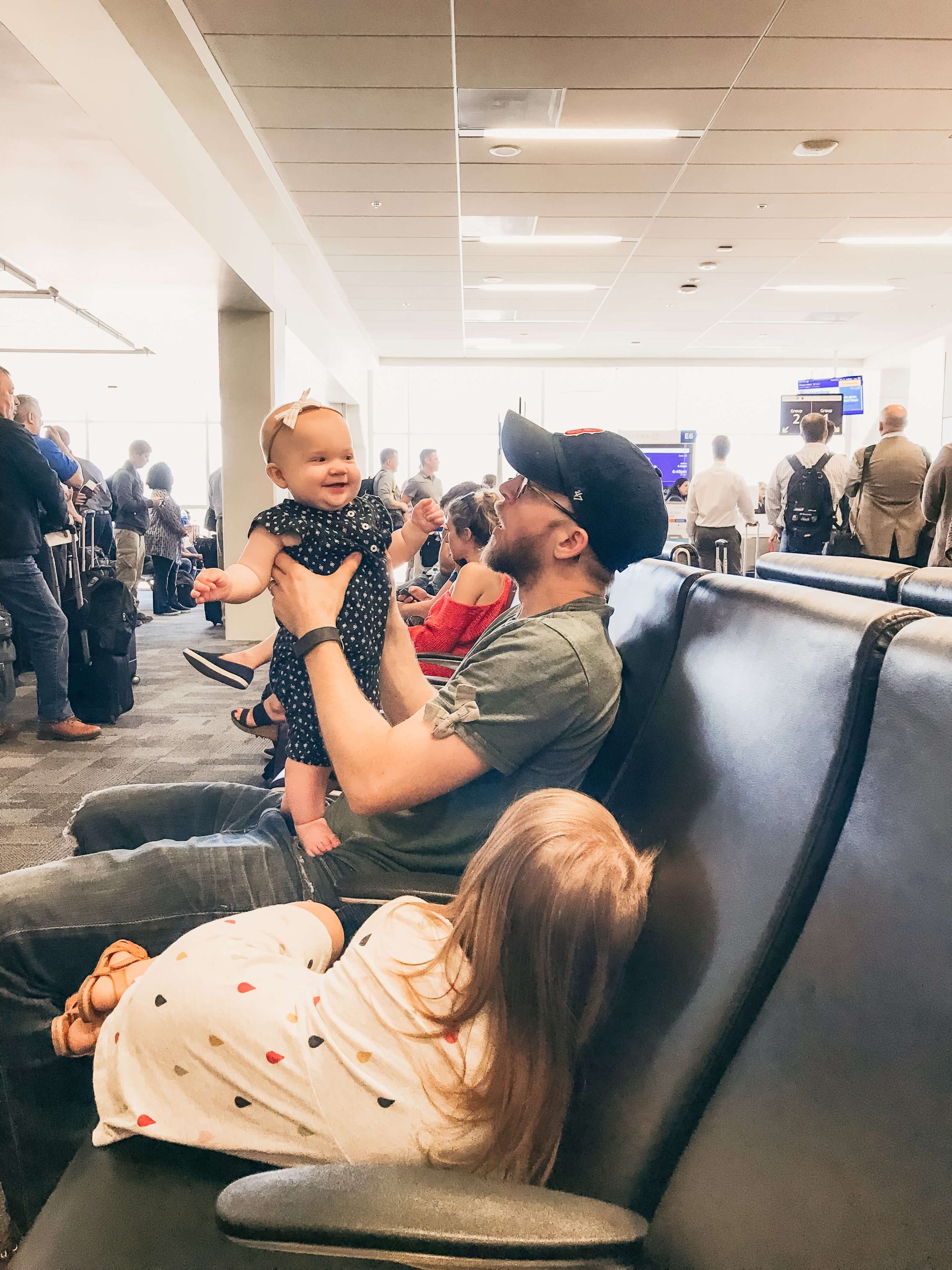 man in a hat holding a baby in the waiting area of an airport