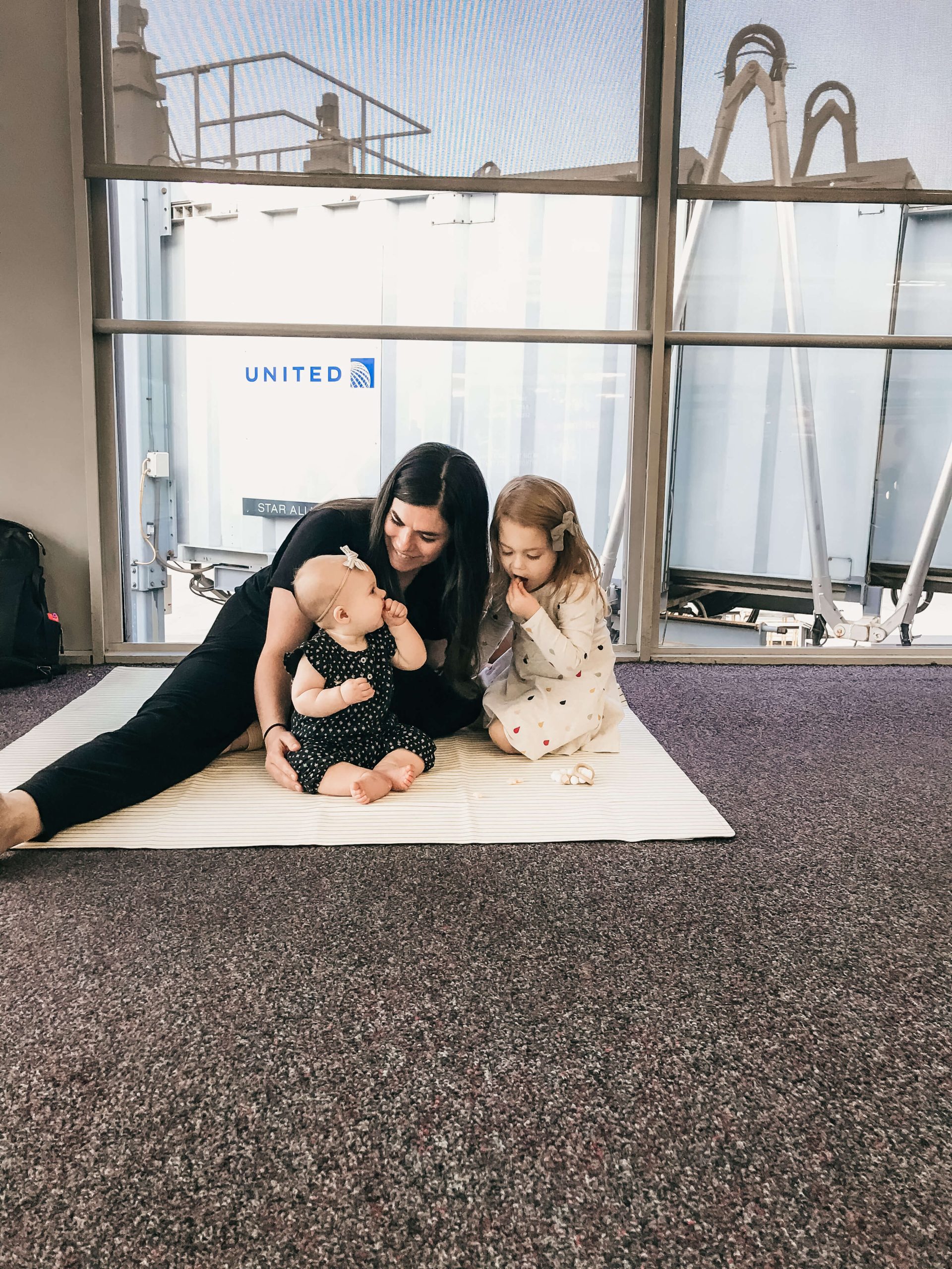 woman and 2 children sitting on the floor in an airport