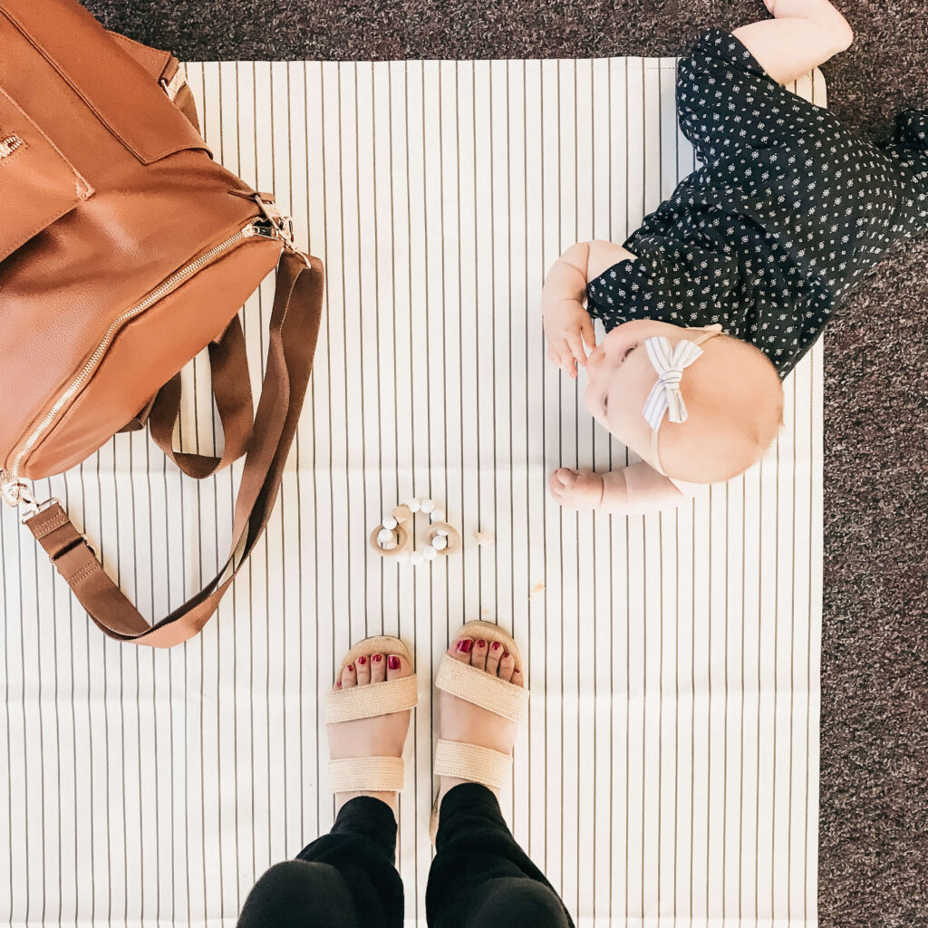 bird's eye view of woman's feet with a baby on a mat and her bag sitting on it