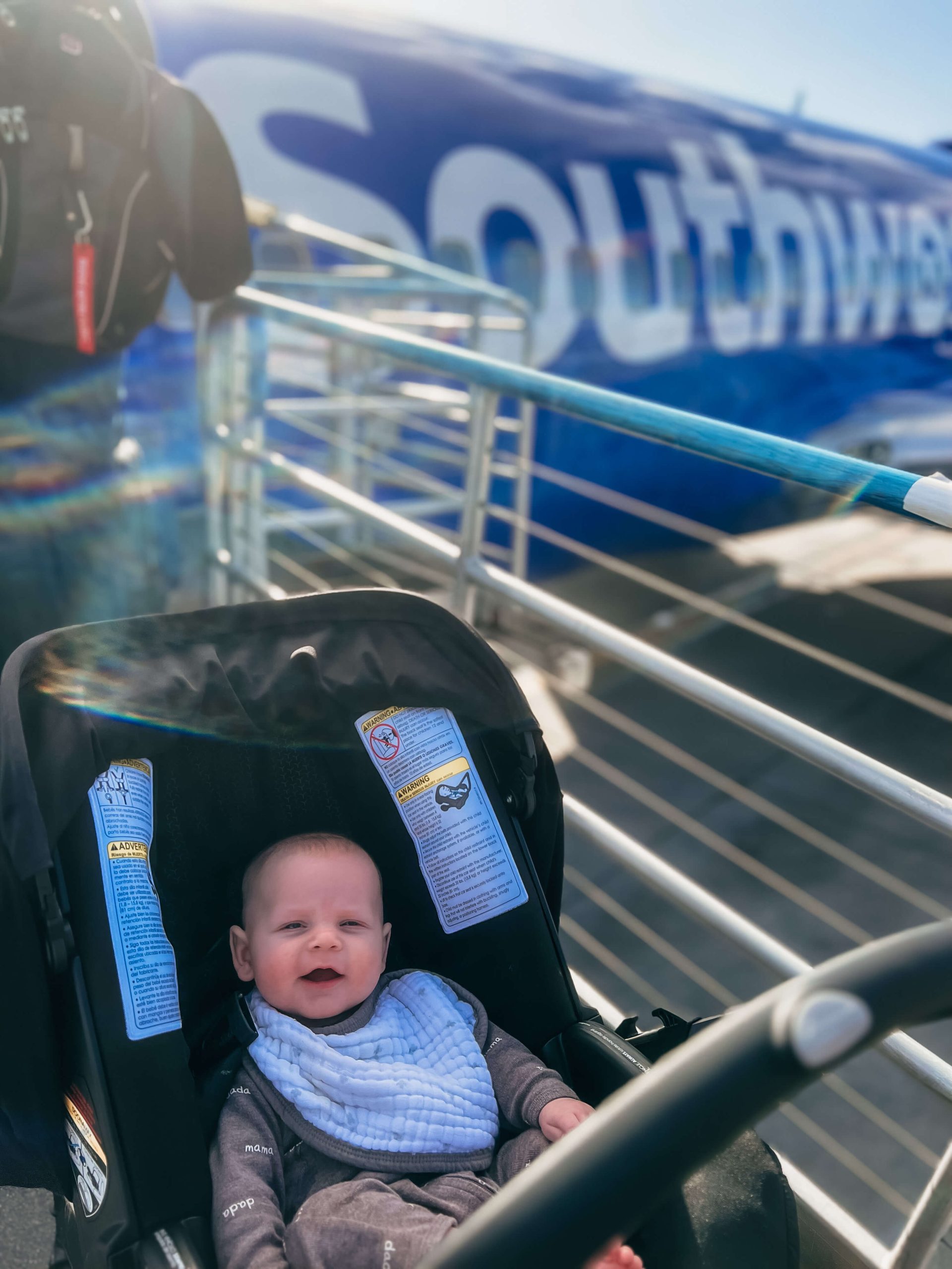 baby in a stroller in clip on burp cloth in front of a southwest airplane