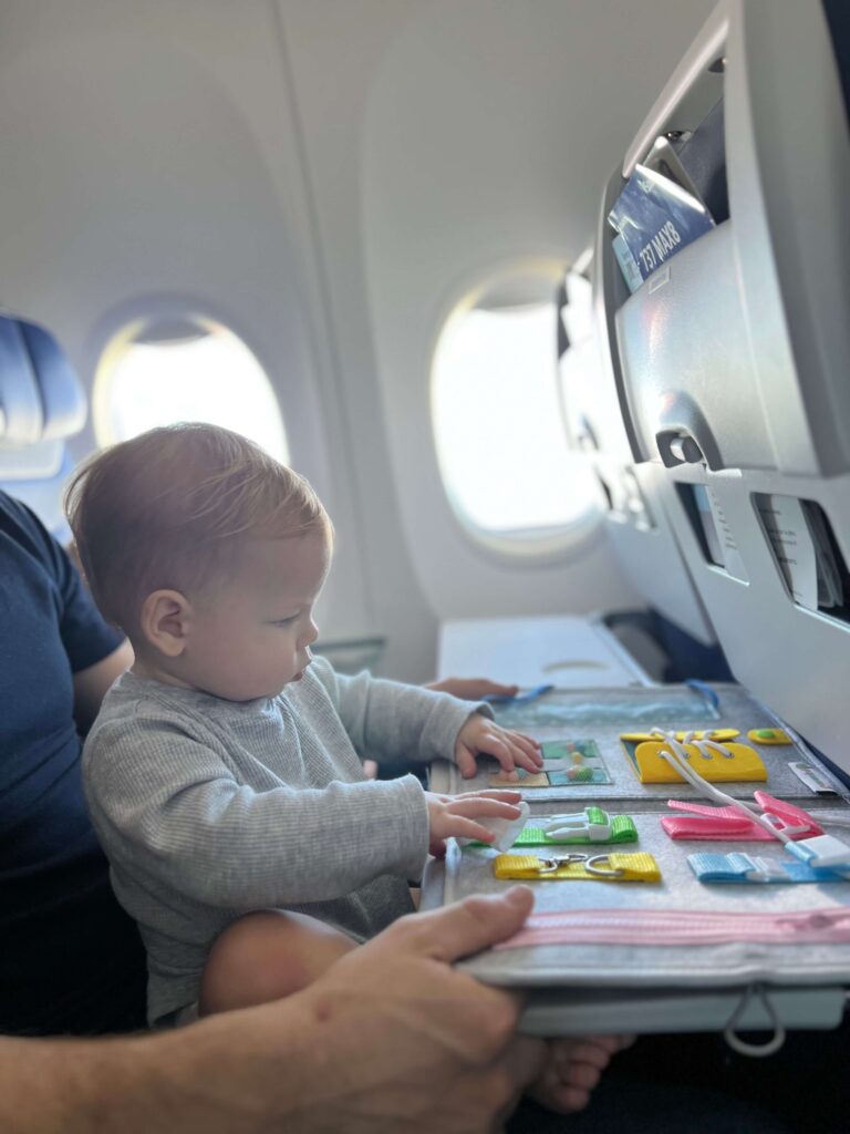 little boy sitting in his mom's lap on an airplane seat playing a game on the tray table