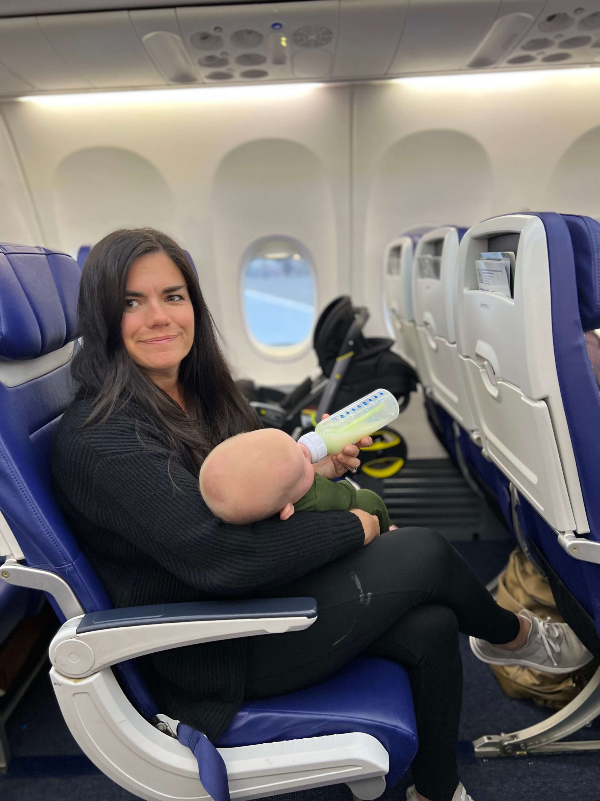 brunette woman feeding a baby a bottle in an airplane