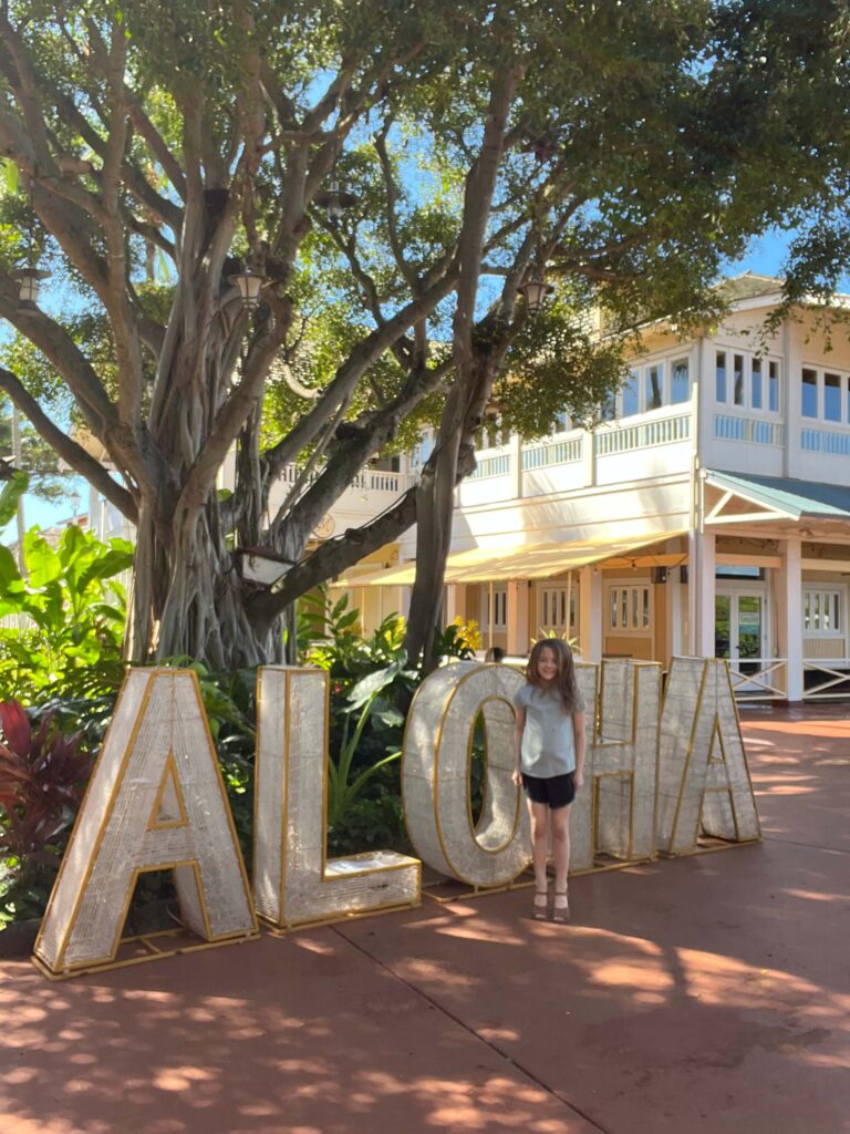 little girl standing in front of te Aloha sign