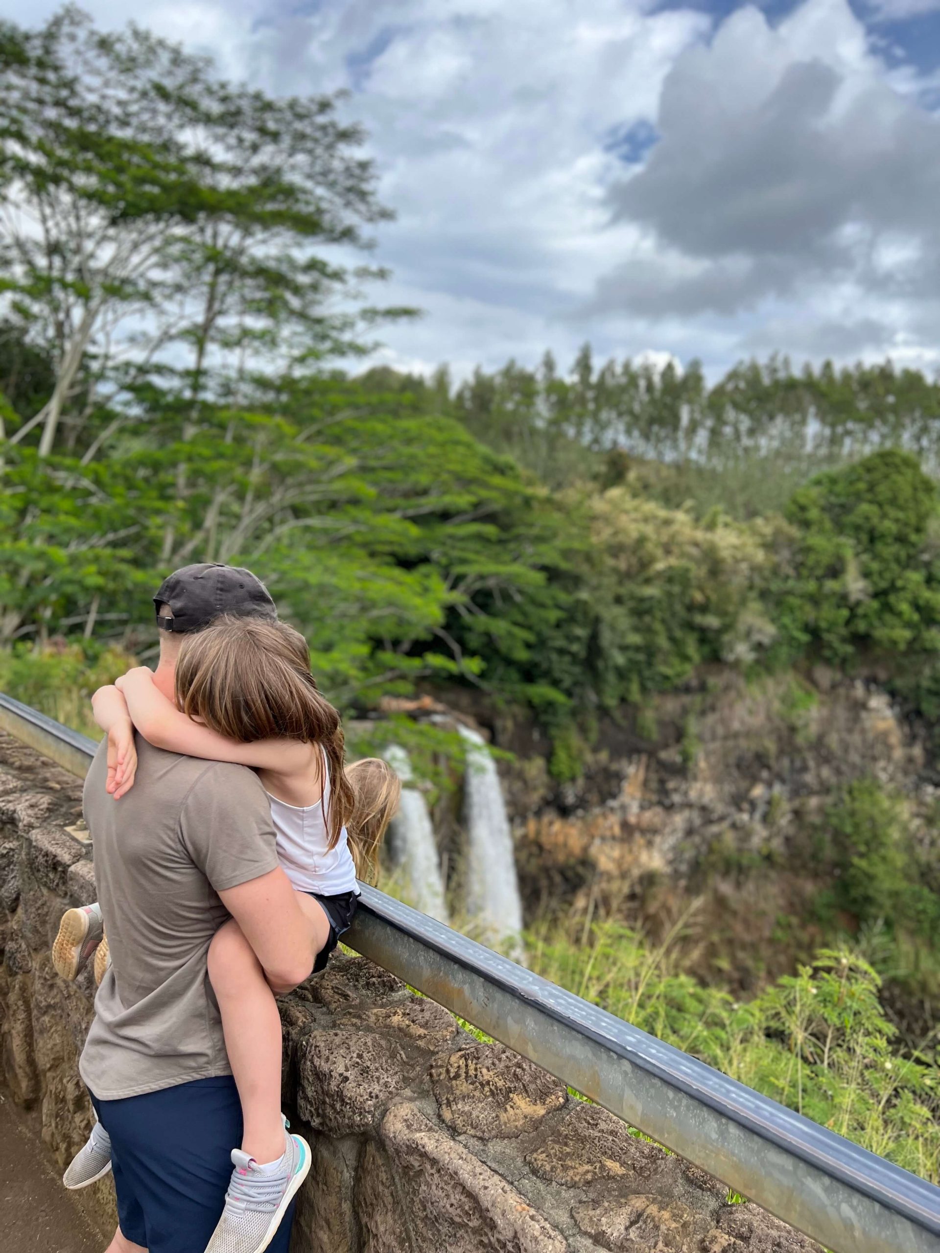 man holding his daughter at waterfall in kauai